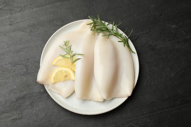 Photo of Uncooked squids with lemon slices and rosemary on black table, top view
