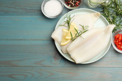 Photo of Uncooked squids with lemon slices, rosemary and spices on blue wooden table, flat lay. Space for text