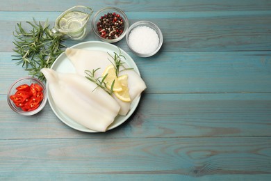 Photo of Uncooked squids with lemon slices, rosemary and spices on blue wooden table, flat lay. Space for text