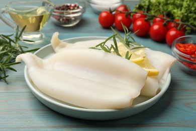 Photo of Uncooked squids with lemon slices, rosemary and spices on blue wooden table, closeup