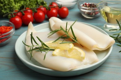 Photo of Uncooked squids with lemon slices, rosemary and spices on blue wooden table, closeup