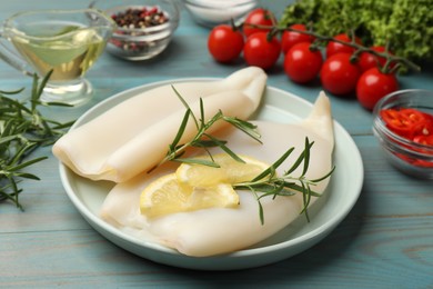 Photo of Uncooked squids with lemon slices, rosemary and spices on blue wooden table, closeup