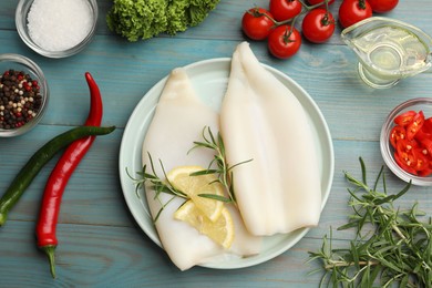 Photo of Uncooked squids with lemon slices, rosemary and spices on blue wooden table, flat lay