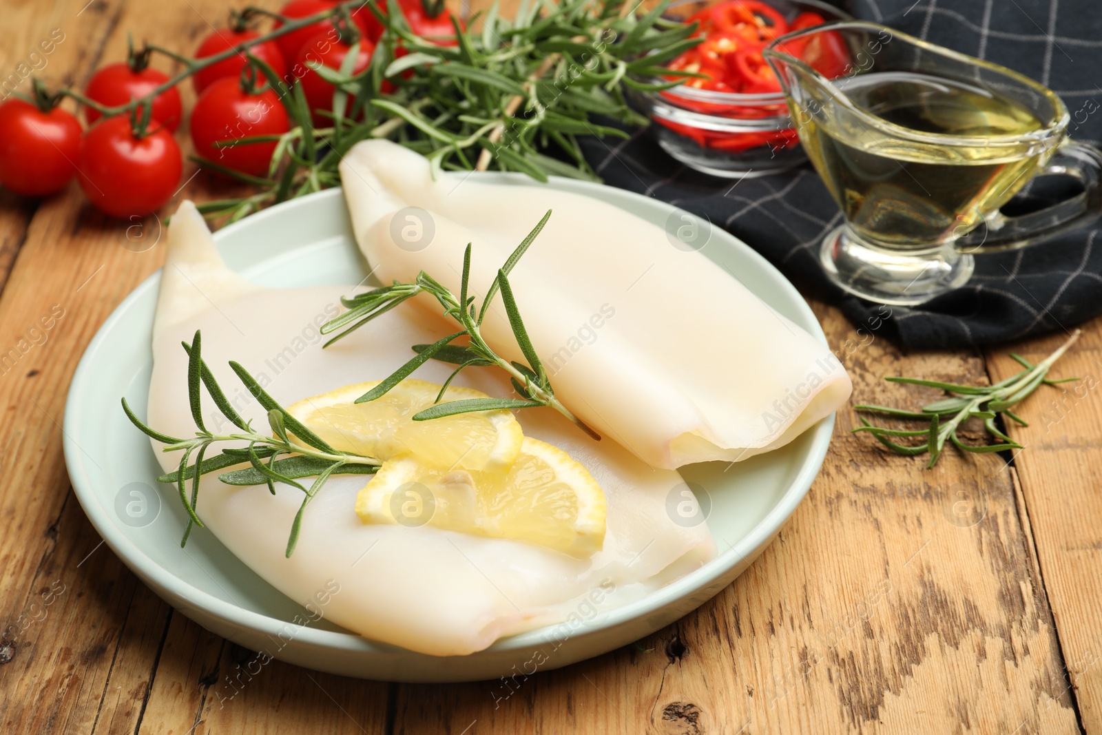 Uncooked squids with lemon slices, rosemary and spices on wooden table, closeup Photo of Uncooked squids with lemon slices, rosemary and spices on wooden table, closeup
