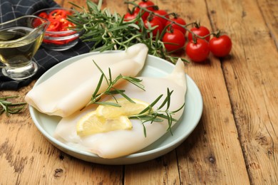 Photo of Uncooked squids with lemon slices, rosemary and spices on wooden table, closeup