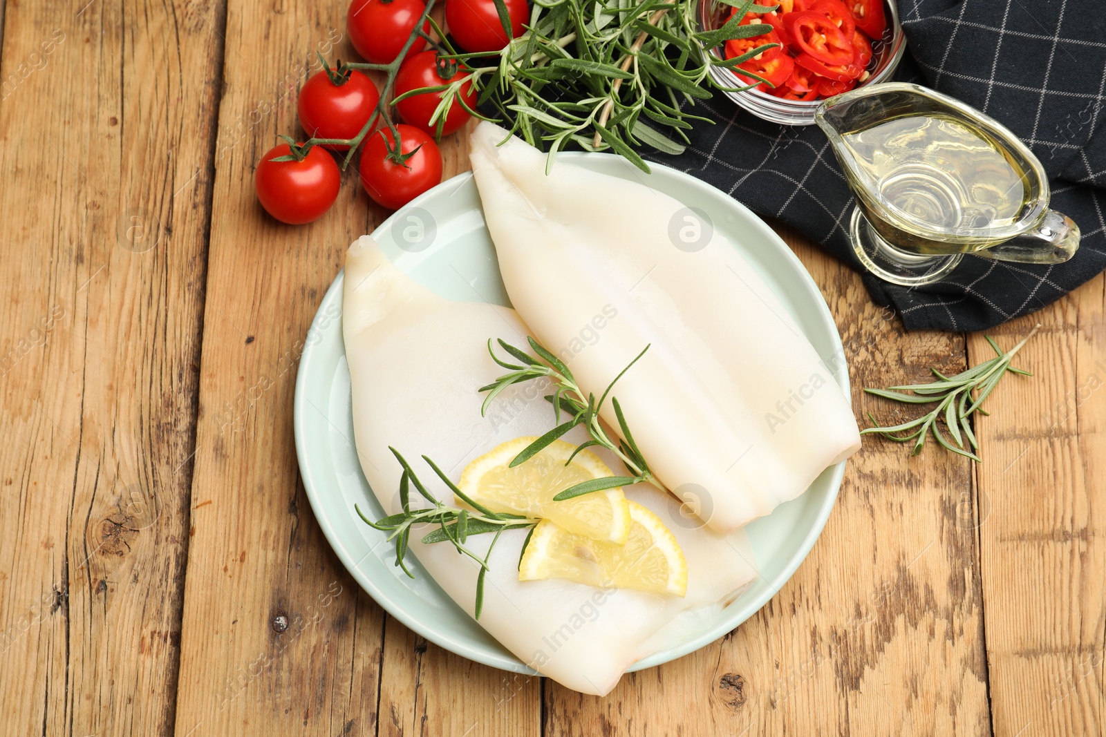 Uncooked squids with lemon slices, rosemary and spices on wooden table, flat lay Photo of Uncooked squids with lemon slices, rosemary and spices on wooden table, flat lay