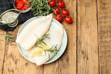 Photo of Uncooked squids with lemon slices, rosemary and spices on wooden table, flat lay. Space for text