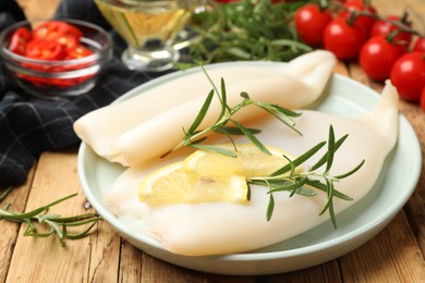 Photo of Uncooked squids with lemon slices, rosemary and spices on wooden table, closeup