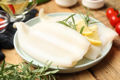 Photo of Uncooked squids with lemon slices, rosemary and spices on wooden table, closeup