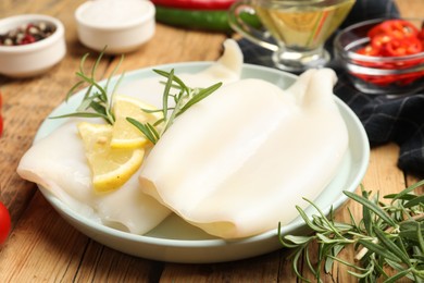 Photo of Uncooked squids with lemon slices, rosemary and spices on wooden table, closeup