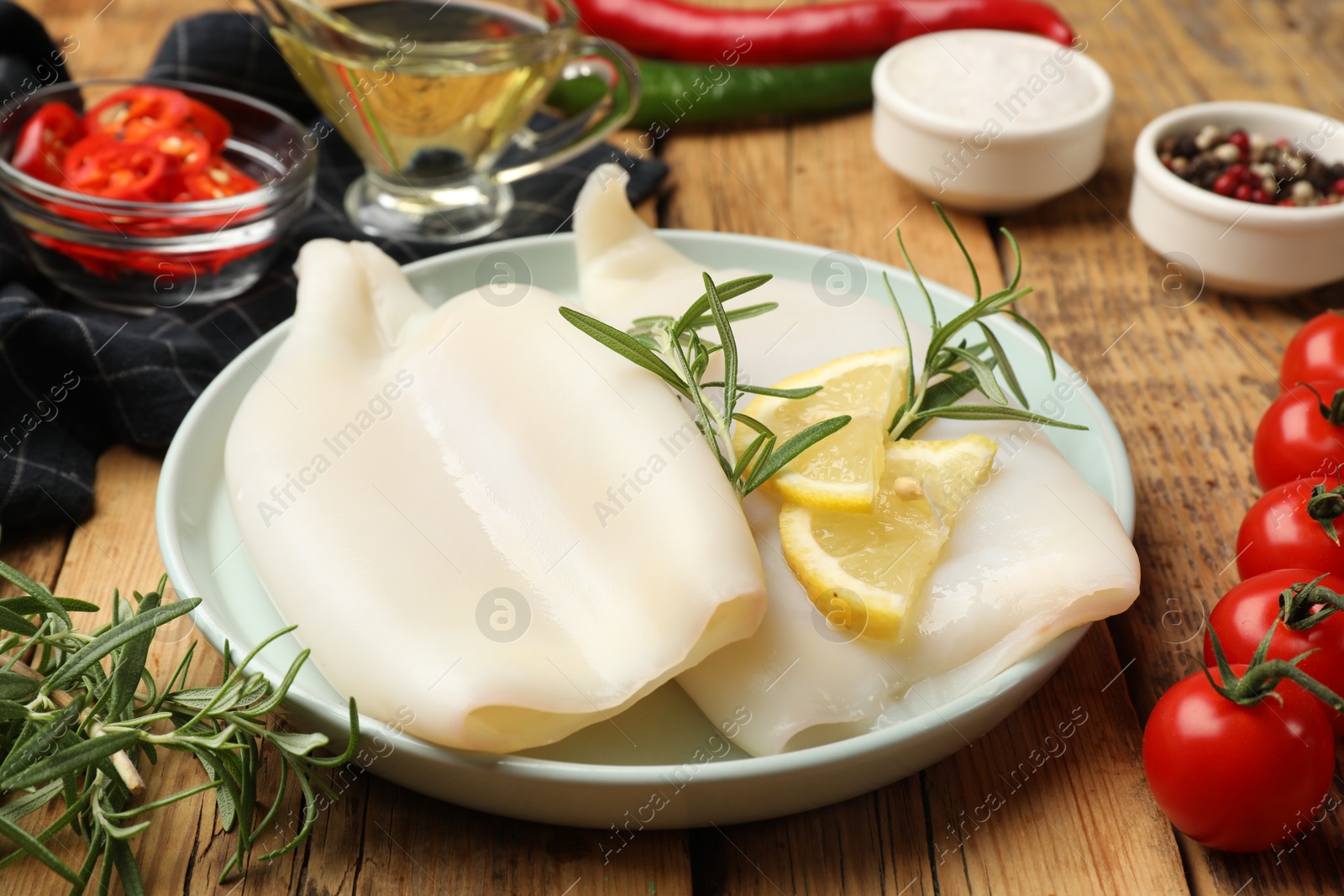 Uncooked squids with lemon slices, rosemary and spices on wooden table, closeup Photo of Uncooked squids with lemon slices, rosemary and spices on wooden table, closeup