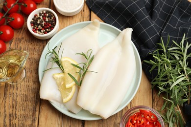 Photo of Uncooked squids with lemon slices, rosemary and spices on wooden table, flat lay