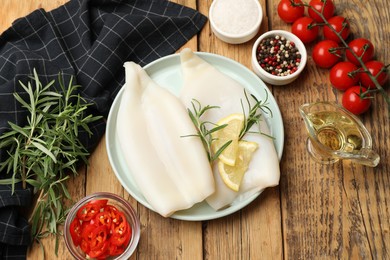 Photo of Uncooked squids with lemon slices, rosemary and spices on wooden table, flat lay