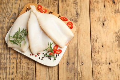 Photo of Uncooked squids with spices on wooden table, top view. Space for text