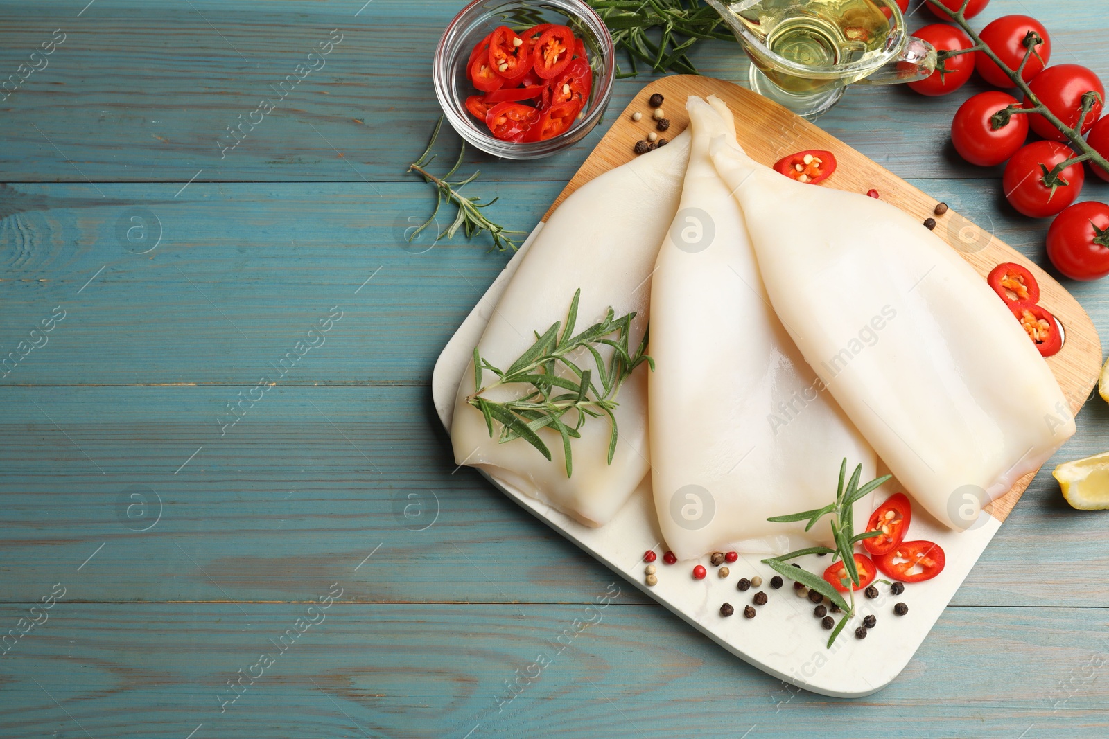 Photo of Uncooked squids with spices on blue wooden table, flat lay. Space for text