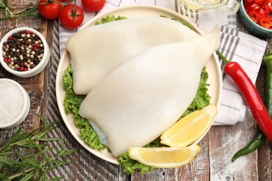 Photo of Uncooked squids with lemon slices, lettuce and spices on wooden table, flat lay