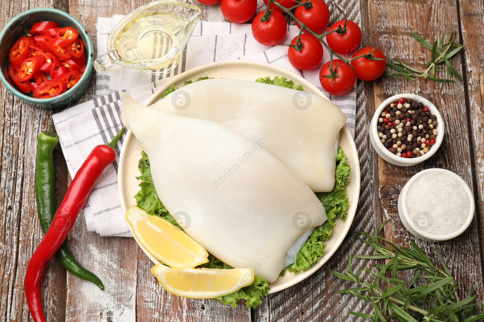 Photo of Uncooked squids with lemon slices, lettuce and spices on wooden table, flat lay