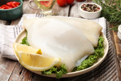 Photo of Uncooked squids with lemon slices, lettuce and spices on wooden table, closeup