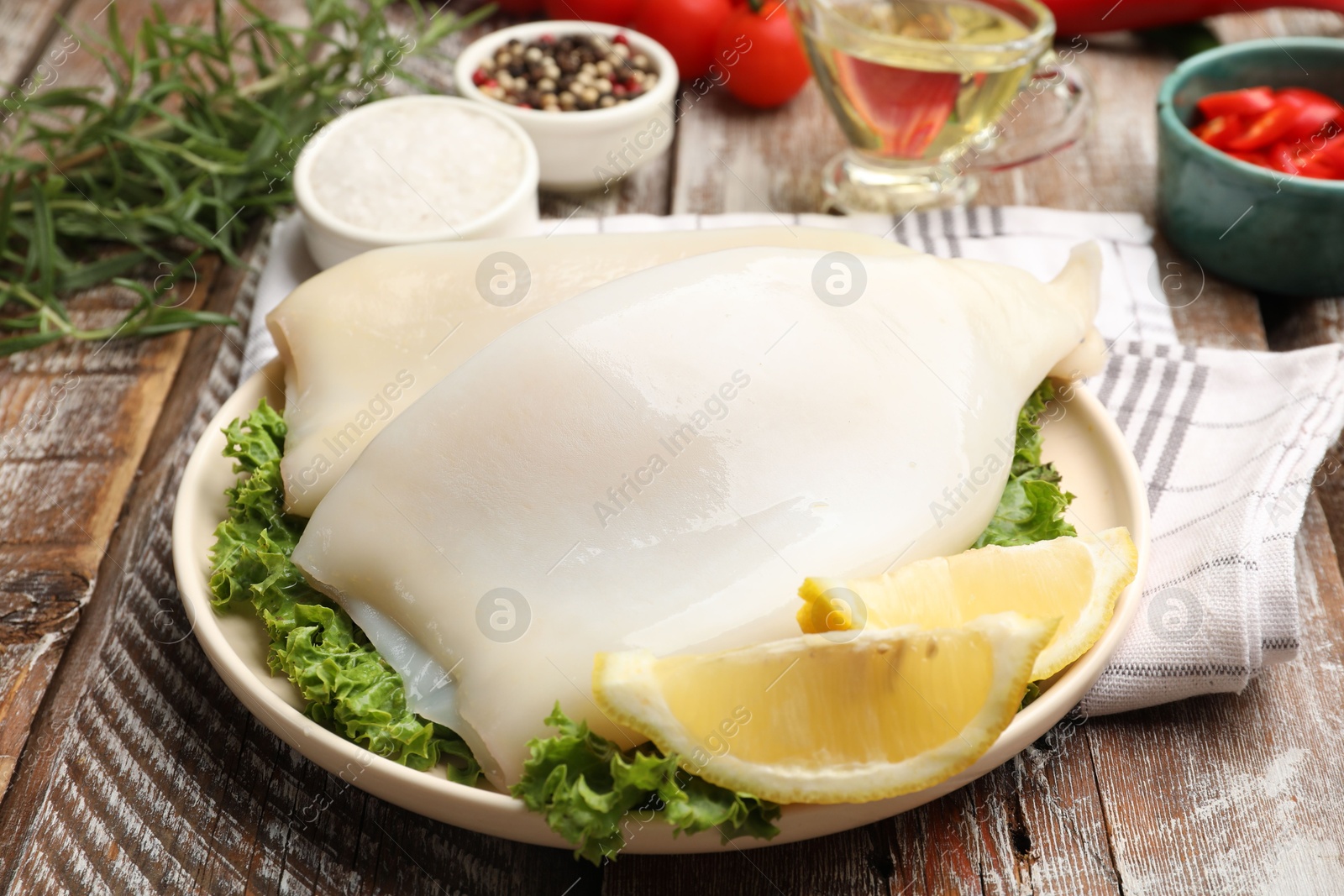 Uncooked squids with lemon slices, lettuce and spices on wooden table, closeup Photo of Uncooked squids with lemon slices, lettuce and spices on wooden table, closeup