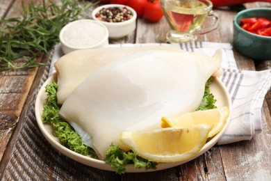 Photo of Uncooked squids with lemon slices, lettuce and spices on wooden table, closeup