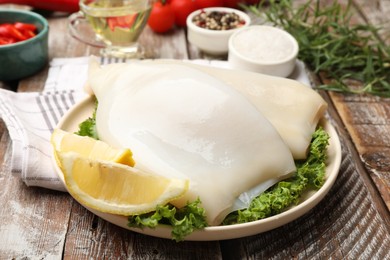 Photo of Uncooked squids with lemon slices, lettuce and spices on wooden table, closeup