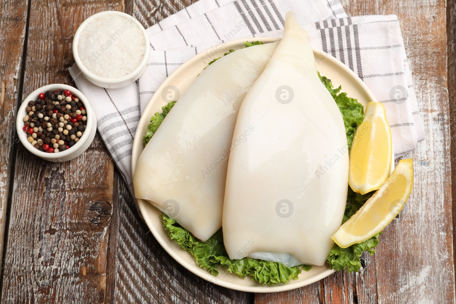 Photo of Uncooked squids with lemon slices, lettuce and spices on wooden table, flat lay