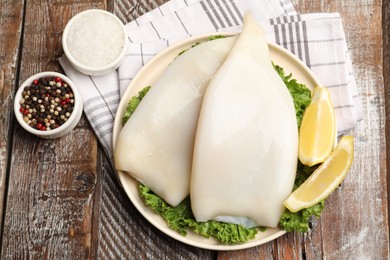 Photo of Uncooked squids with lemon slices, lettuce and spices on wooden table, flat lay