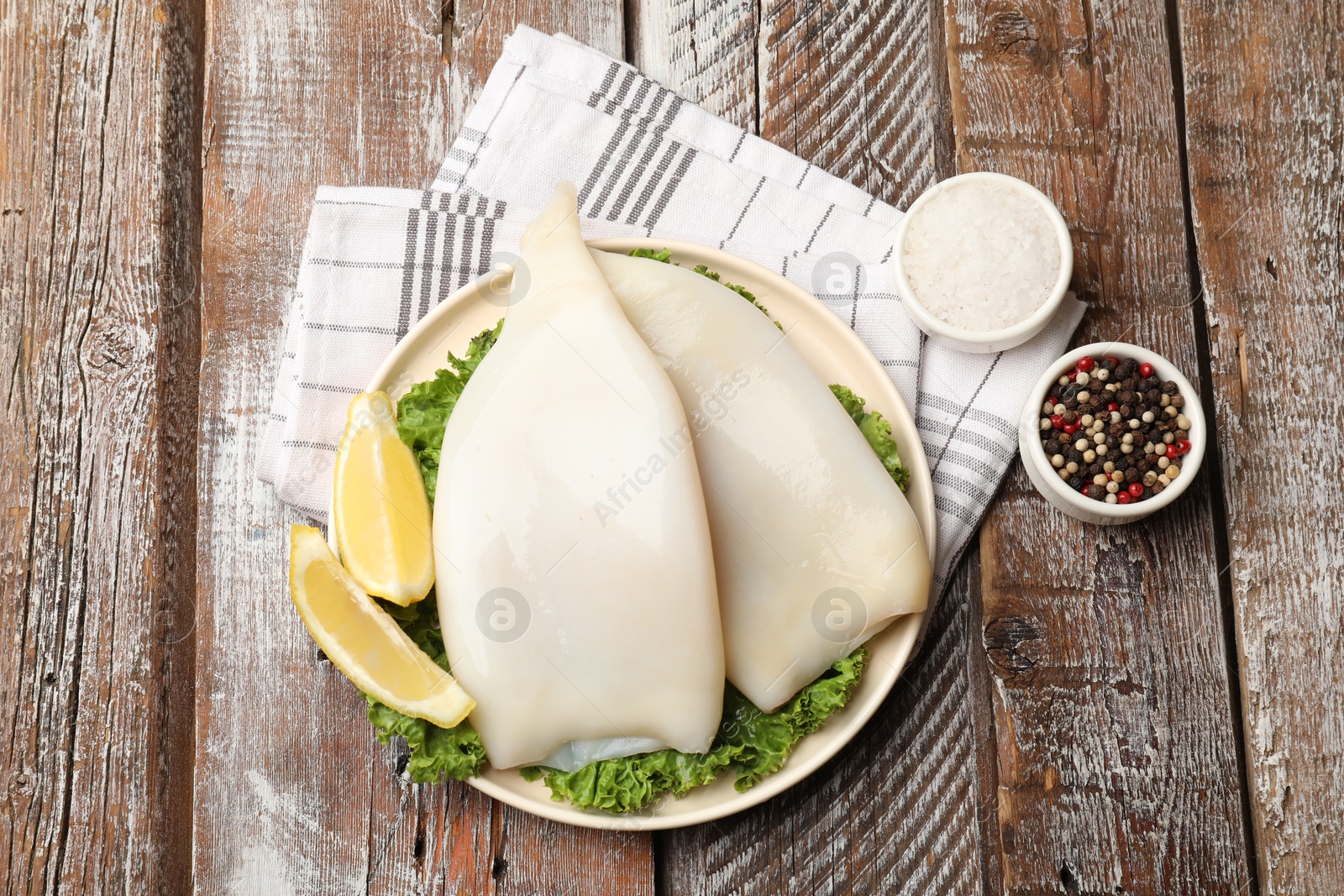 Photo of Uncooked squids with lemon slices, lettuce and spices on wooden table, flat lay
