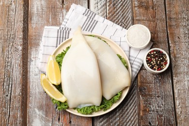 Photo of Uncooked squids with lemon slices, lettuce and spices on wooden table, flat lay