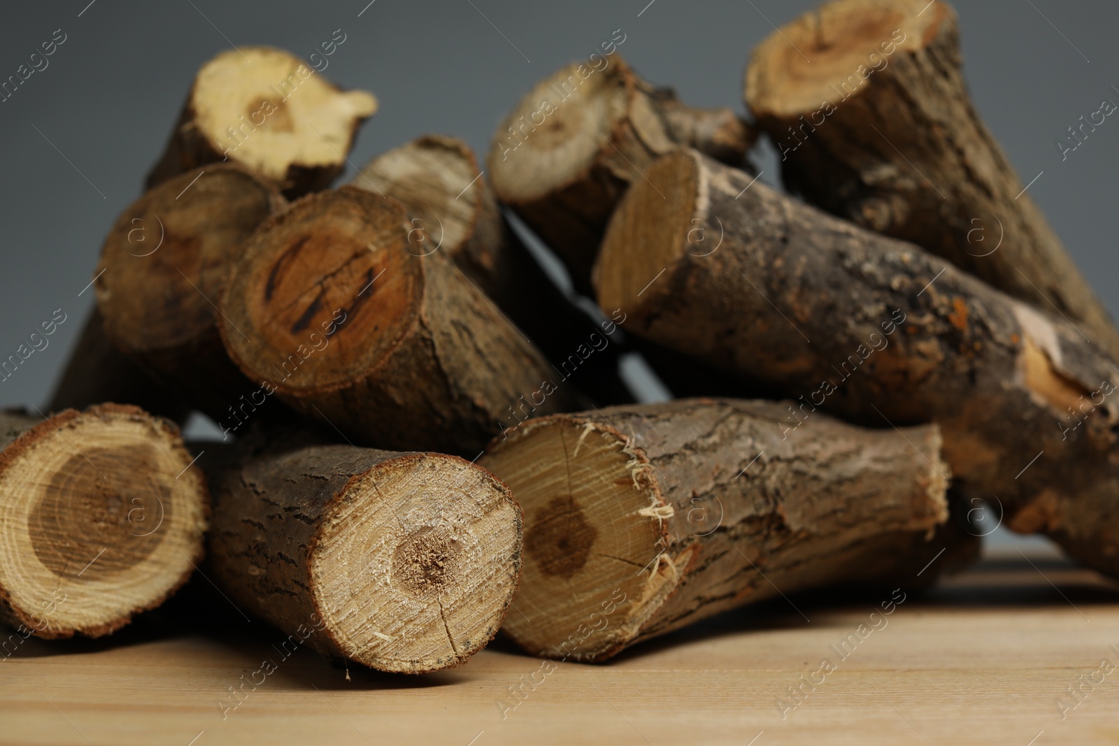 Photo of Pile of cut firewood on wooden table against grey background, closeup