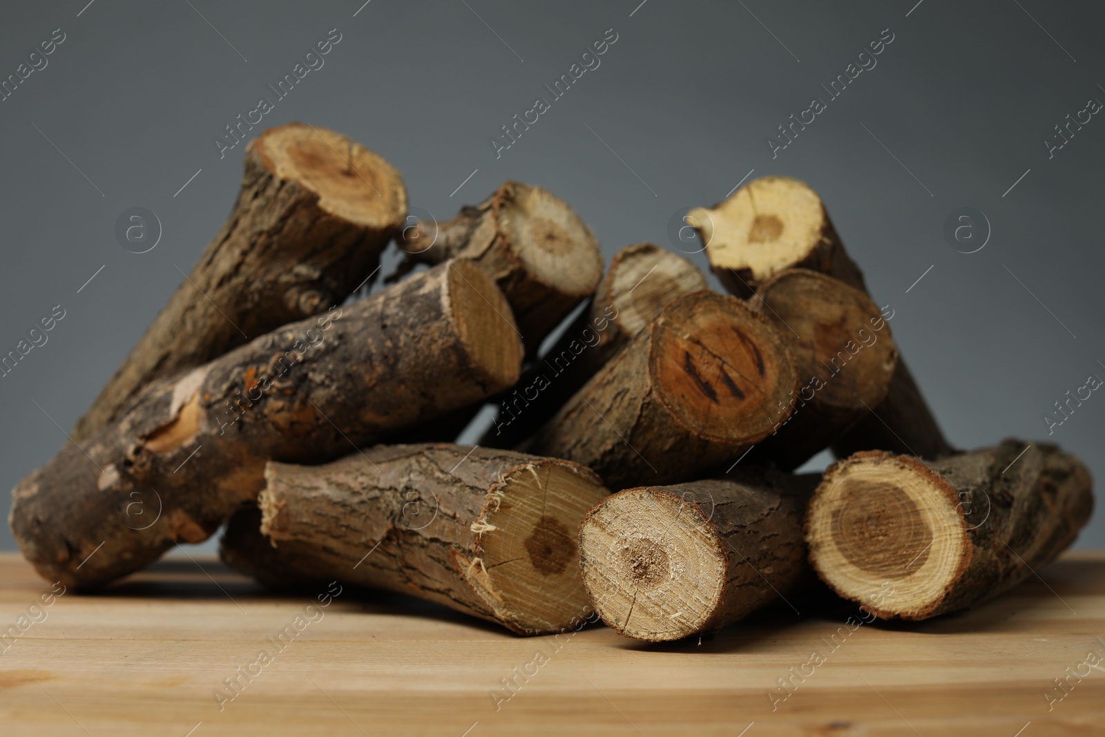Photo of Pile of cut firewood on wooden table against grey background, closeup