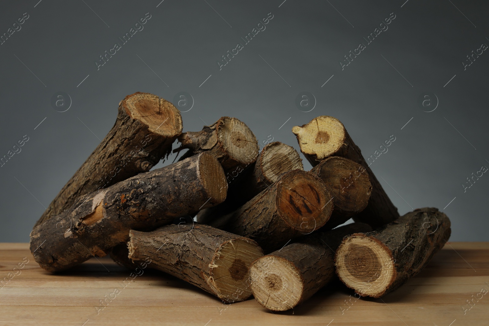 Photo of Pile of cut firewood on wooden table against grey background, closeup