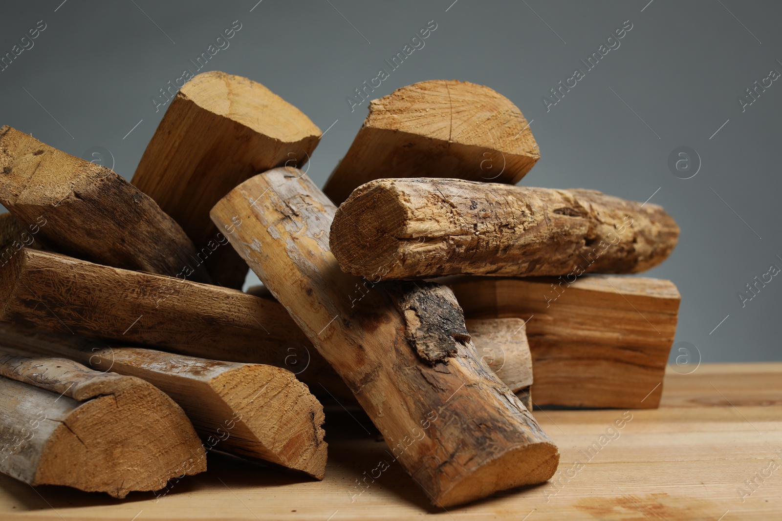Photo of Pile of cut firewood on wooden table against grey background, closeup