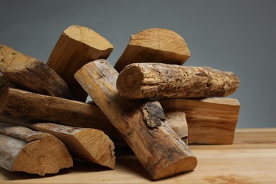 Photo of Pile of cut firewood on wooden table against grey background, closeup