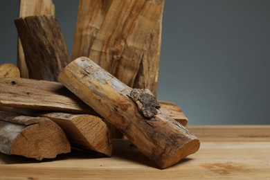 Photo of Pile of cut firewood on wooden table against grey background, closeup. Space for text