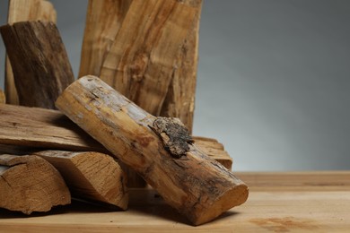 Photo of Pile of cut firewood on wooden table against grey background, closeup. Space for text