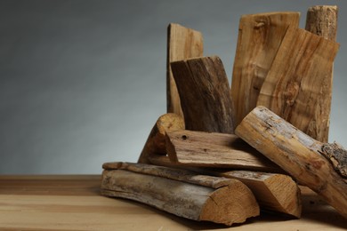 Photo of Pile of cut firewood on wooden table against grey background, closeup. Space for text