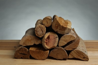 Photo of Pile of cut firewood on wooden table against grey background, closeup