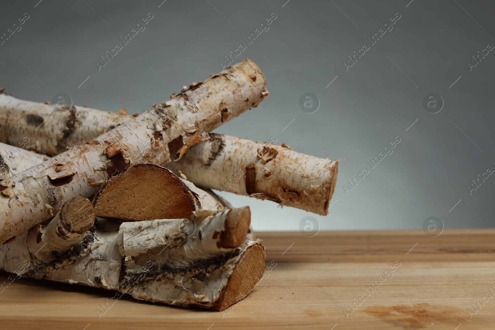 Pile of cut firewood on wooden table against grey background, closeup. Space for text Photo of Pile of cut firewood on wooden table against grey background, closeup. Space for text