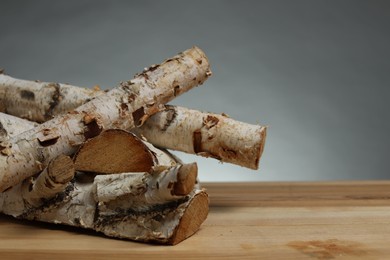 Photo of Pile of cut firewood on wooden table against grey background, closeup. Space for text