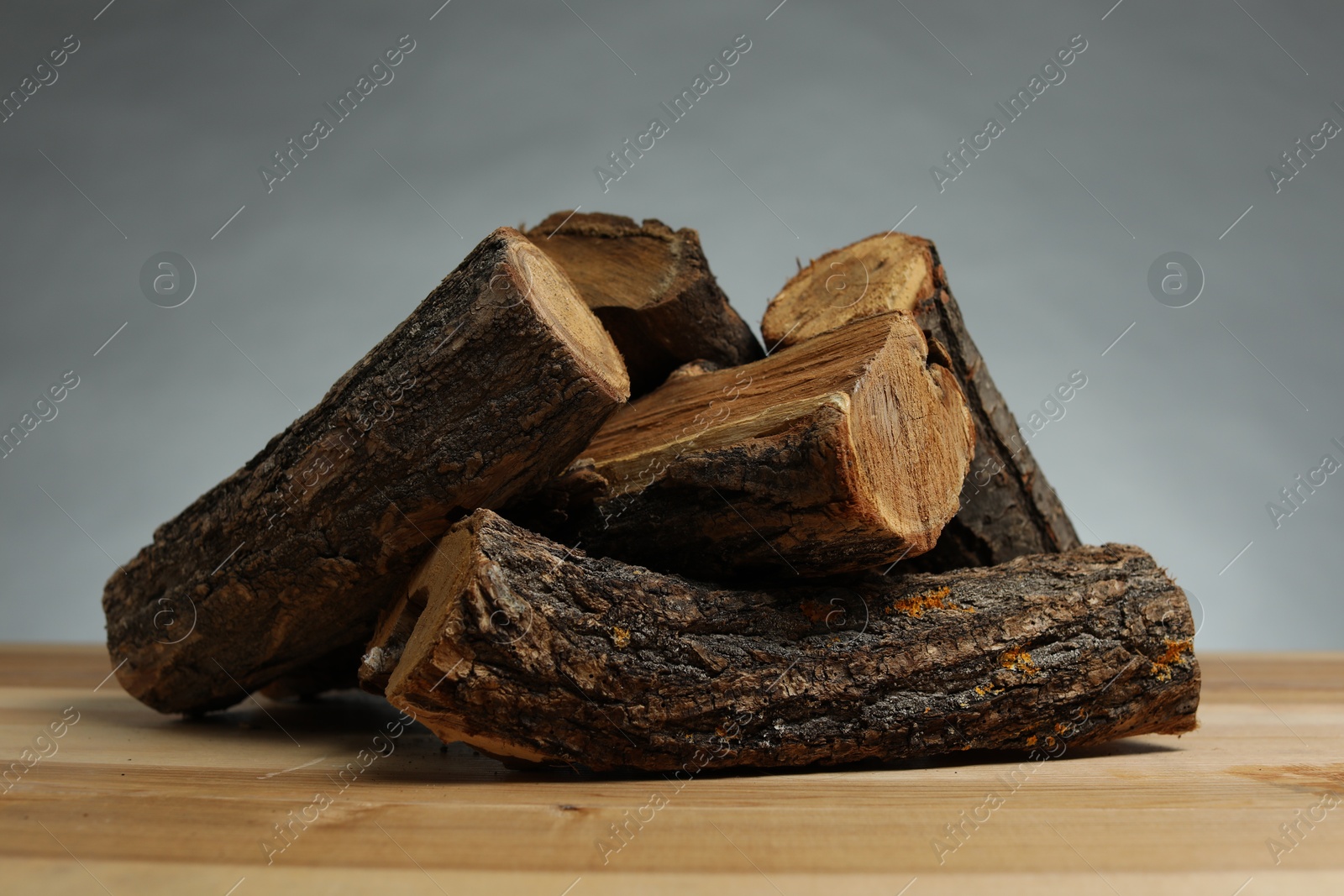 Photo of Pile of cut firewood on wooden table against grey background