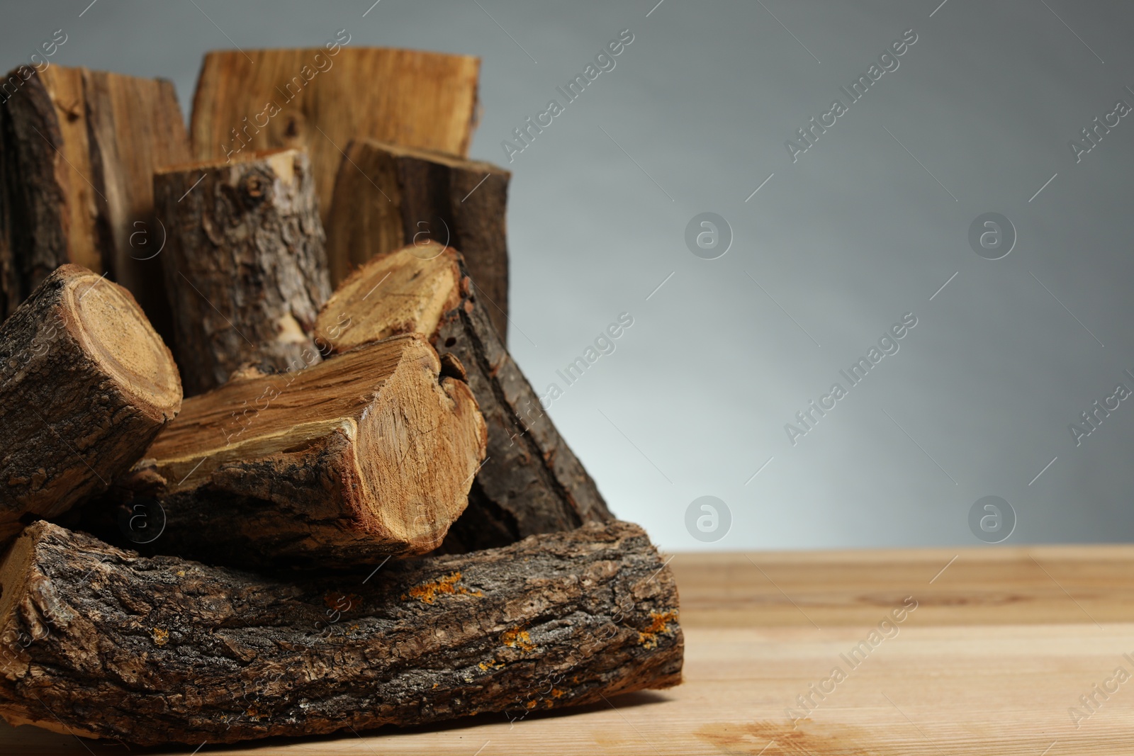 Pile of cut firewood on wooden table against grey background, closeup. Space for text Photo of Pile of cut firewood on wooden table against grey background, closeup. Space for text