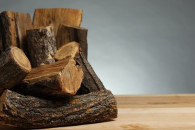 Photo of Pile of cut firewood on wooden table against grey background, closeup. Space for text