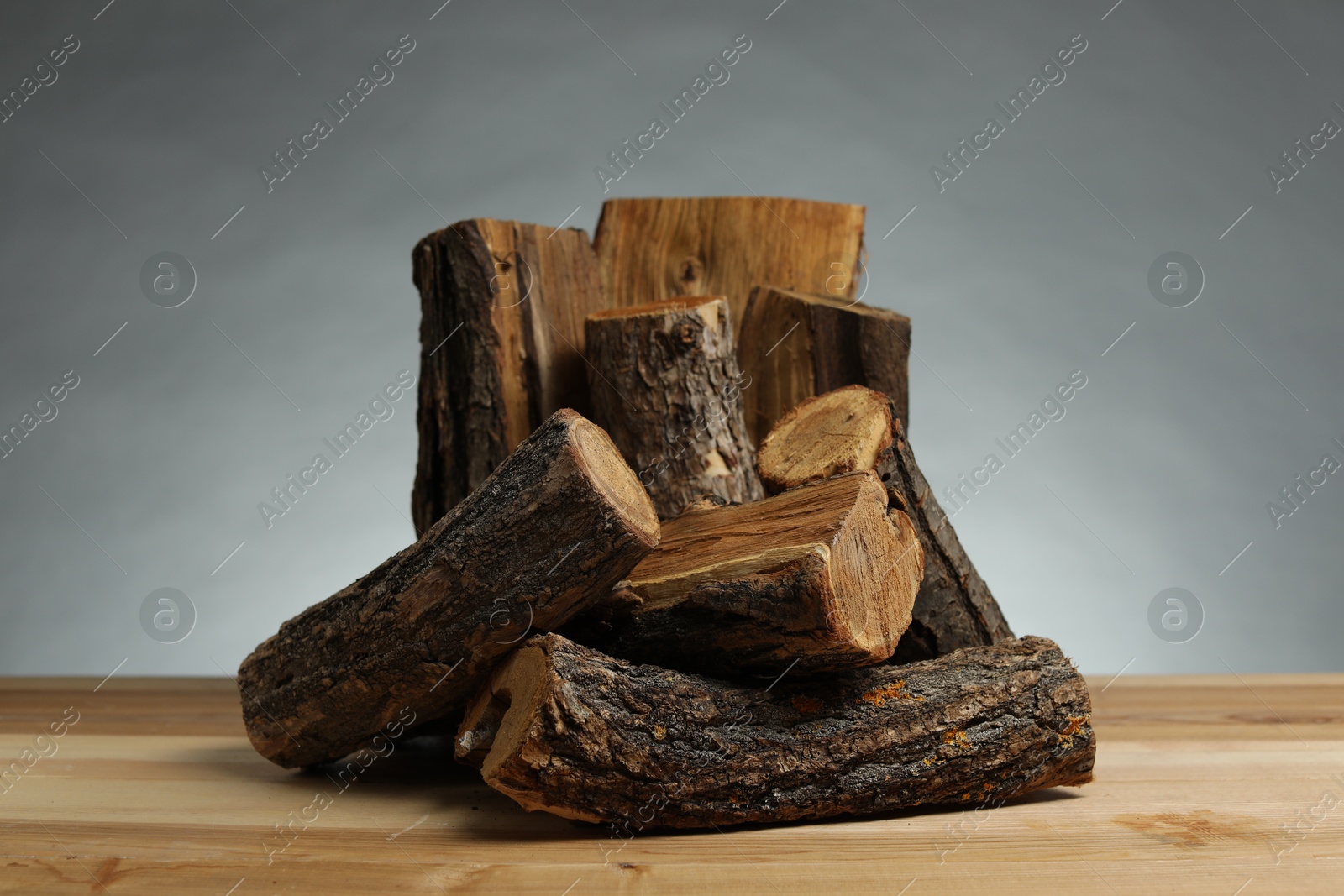 Pile of cut firewood on wooden table against grey background Photo of Pile of cut firewood on wooden table against grey background