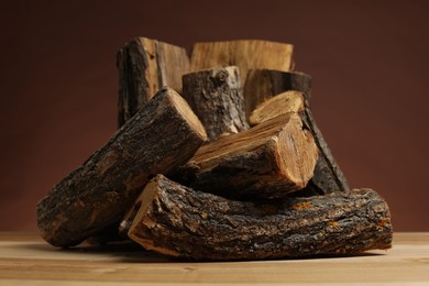 Photo of Pile of cut firewood on wooden table against brown background, closeup