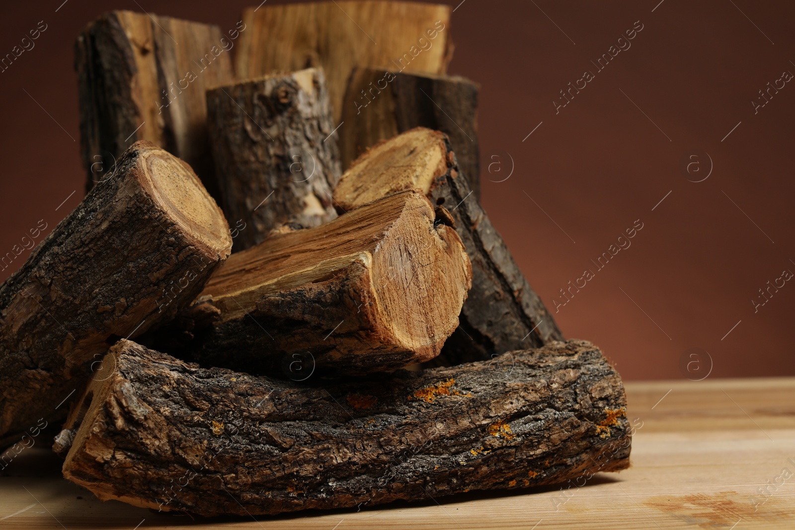 Photo of Pile of cut firewood on wooden table against brown background, closeup. Space for text