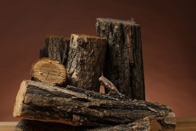 Photo of Pile of cut firewood on table against brown background, closeup