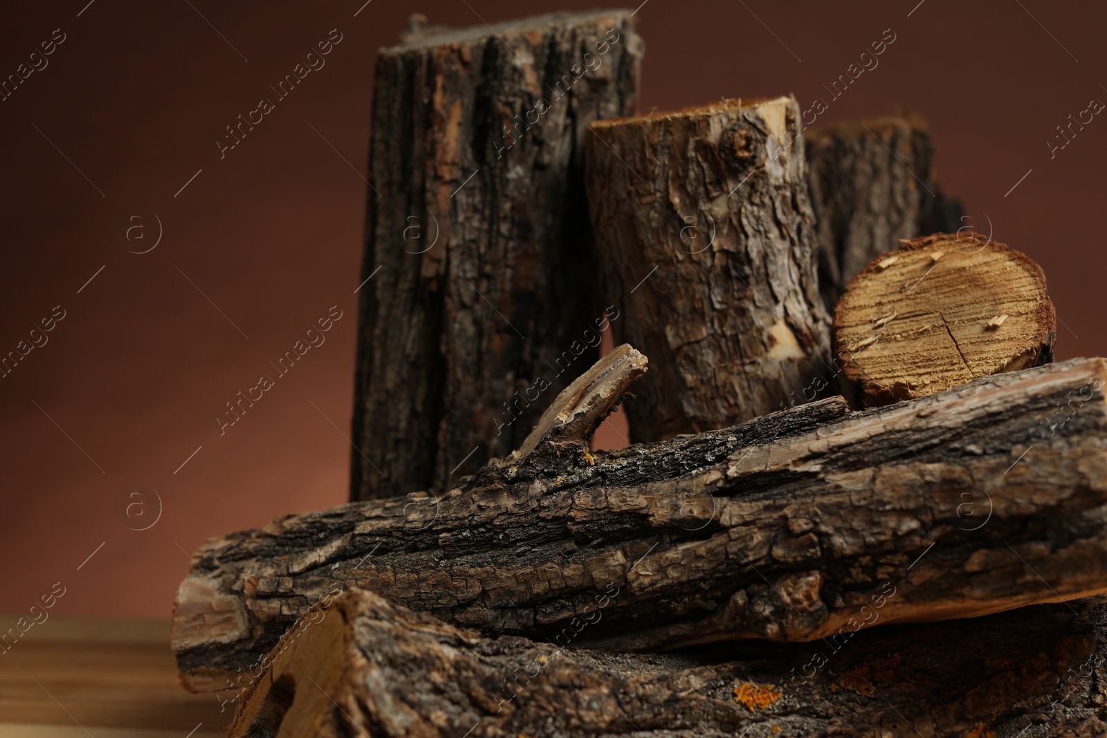 Photo of Pile of cut firewood on table against brown background, closeup