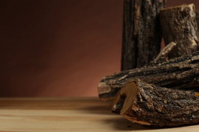 Photo of Pile of cut firewood on wooden table against brown background, closeup. Space for text