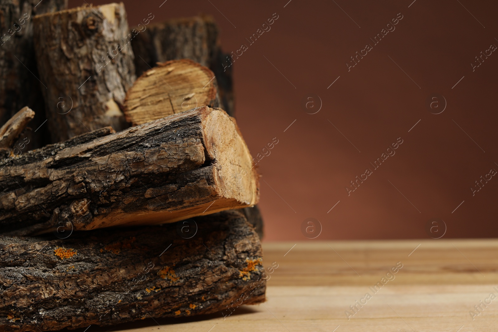 Photo of Pile of cut firewood on wooden table against brown background, closeup. Space for text